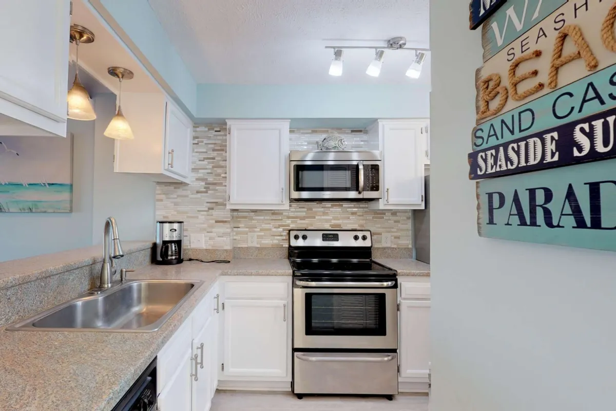 A relaxed kitchen setting with stainless steel appliances, a granite countertop, and beach-themed decor. The space feels casual yet functional, ideal for preparing meals and entertaining guests in a coastal atmosphere.