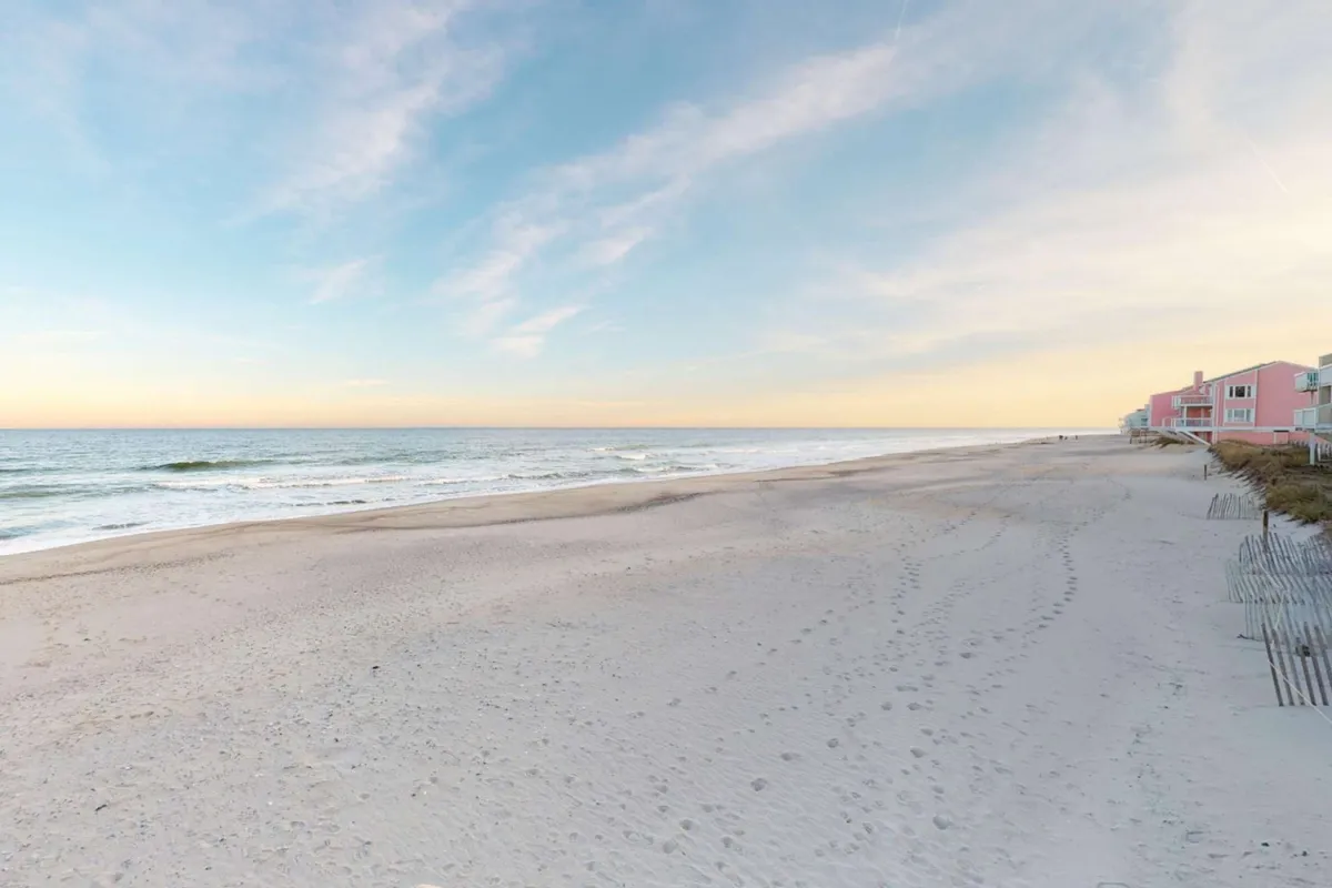 This image features an expansive beach bordered by ocean waves and colorful beachfront houses under a relaxed coastal sky. The broad shoreline invites leisurely walks and the gentle surf sets a tranquil scene, perfect for enjoying the mild climate Kure Beach is known for.