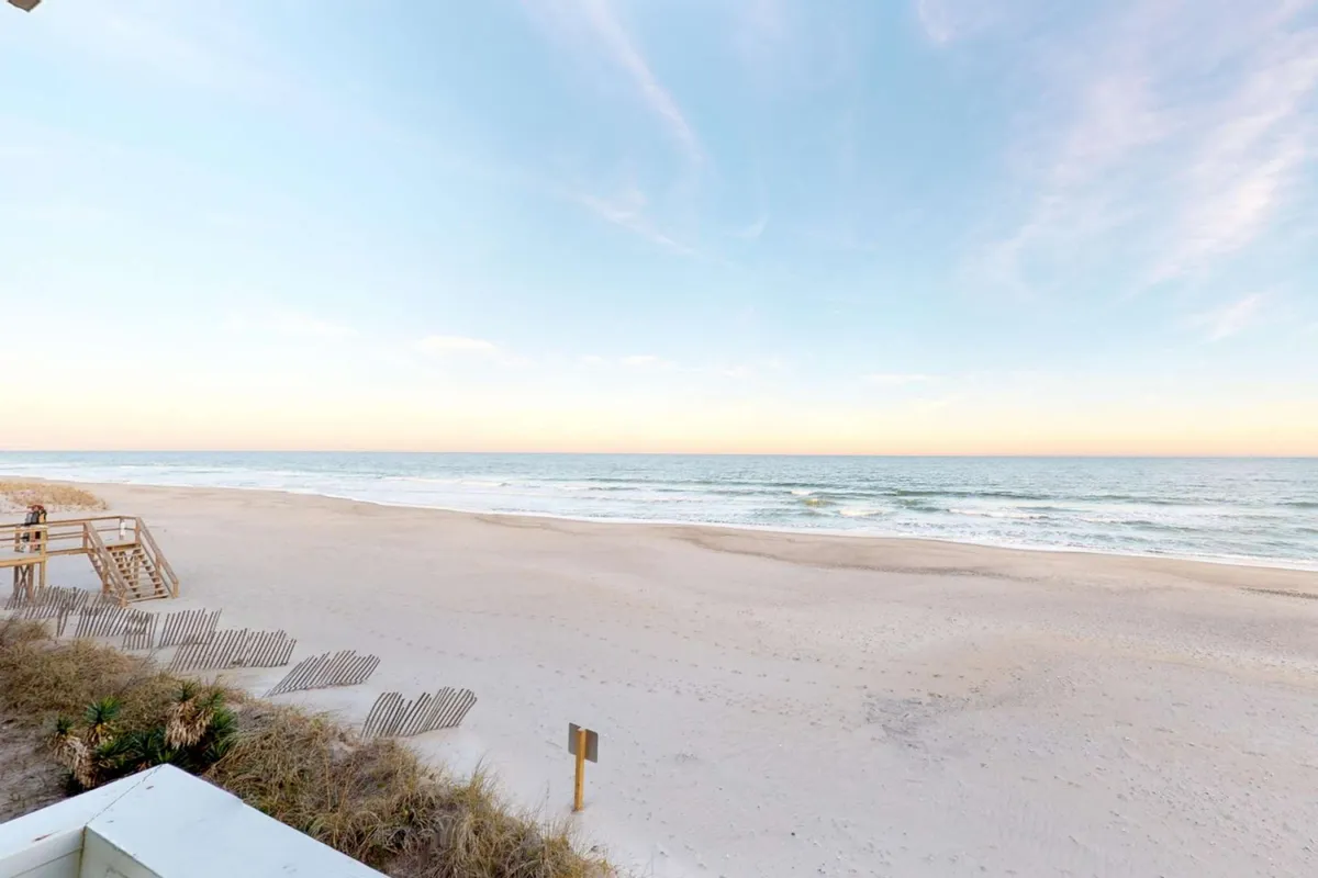 The hero image features a breathtaking, unobstructed view of the Atlantic Ocean from the beachfront condo at Ocean Dunes Resort. The scene showcases rolling dunes and a wide sandy beach stretching out to meet the sparkling blue water under an expansive sky, evoking a peaceful, sun-drenched atmosphere ideal for relaxation and seaside activities.