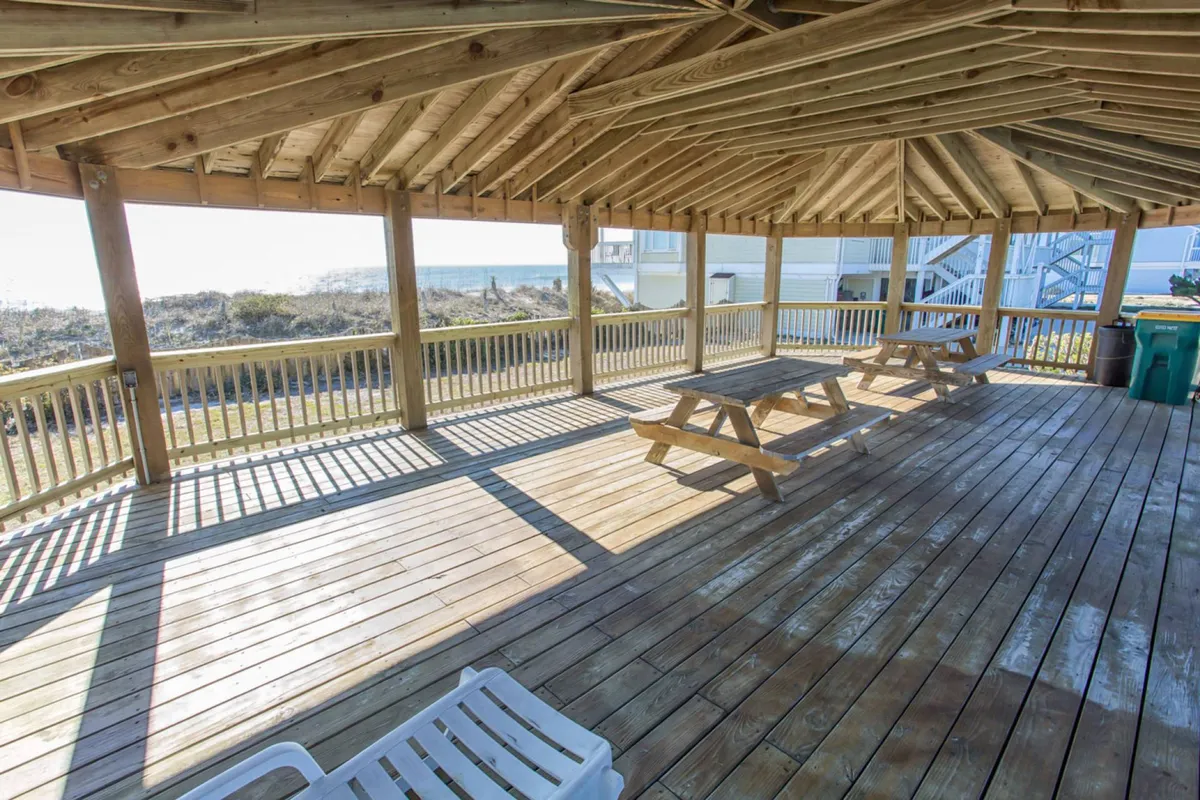 A cheerful gazebo with wooden picnic tables offers open space for gatherings, with views of the beach and ocean beyond. The image conveys a sense of community and the opportunity for outdoor relaxation even in cooler months.