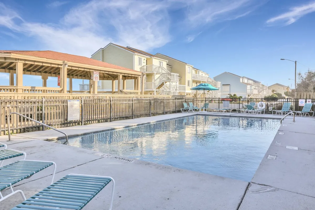 A sparkling outdoor swimming pool surrounded by lounge chairs and a covered pavilion, with the resort’s buildings in the background. The scene suggests leisure and sociability, inviting guests to bask in the sun, enjoy poolside gatherings, and make memories outdoors.