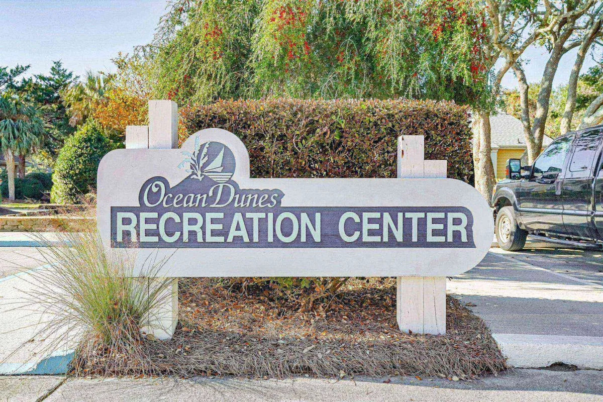 An exterior shot showcasing the Recreation Center’s prominent signage, with lush greenery and a welcoming parking area. The building signals communal activities, family gatherings, and recreational opportunities within the Ocean Dunes community.