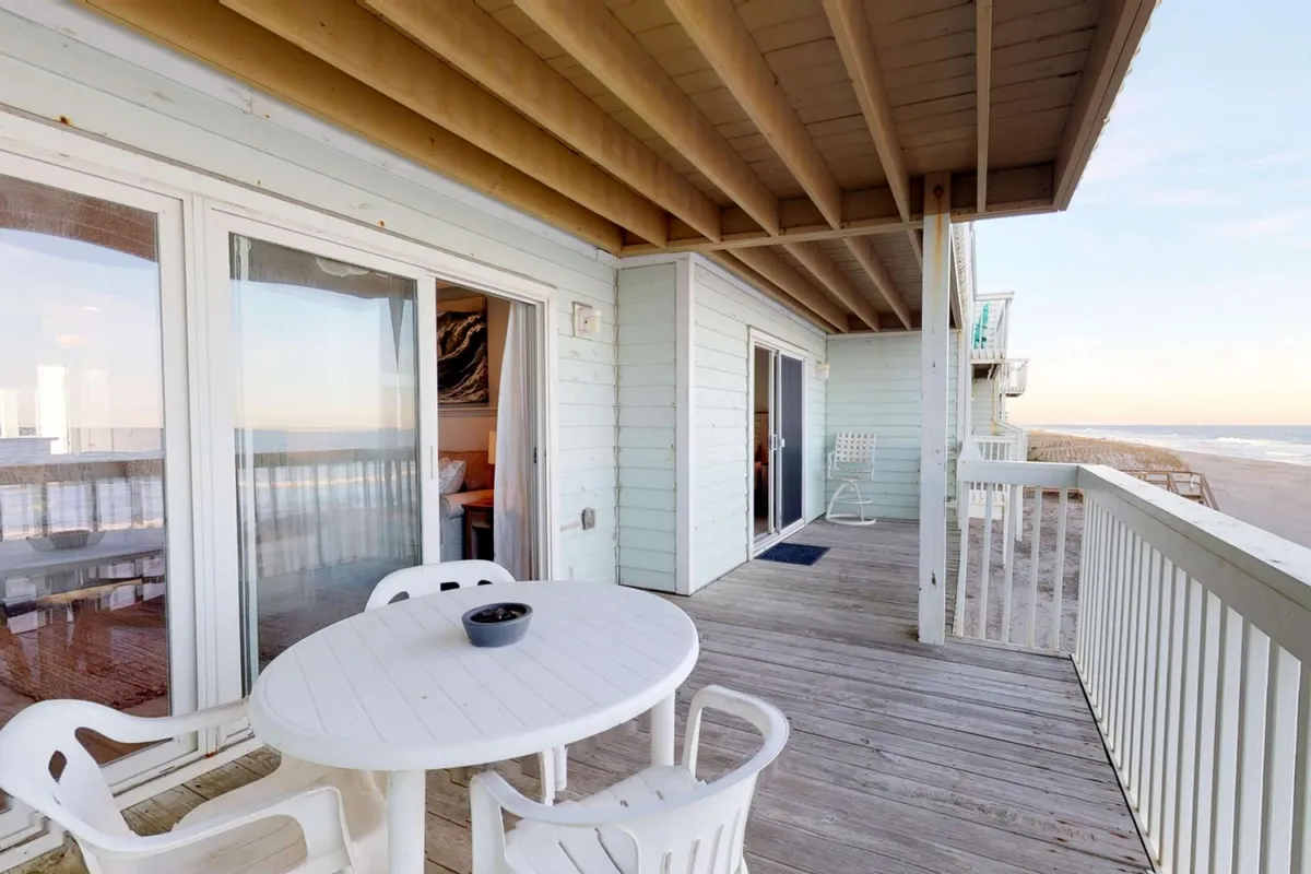 An outdoor table set on a patio or balcony with a direct view of the beach, seen through sliding glass doors. The tranquil setup suggests leisurely breakfasts, sunset viewings, or relaxing with a book—all while enjoying the soothing sights and sounds of the coast.